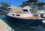 Blue and white motorboat with a tan canvas cover moored at a marina, tied to a dock.