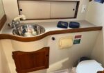 Compact boat head with a stainless sink, curved wood countertop, and a nearby toilet on the right side.