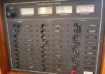 AC/DC master control panel with gauges at top and multiple labeled switch banks for DC/AC power and systems on a wooden frame panel.