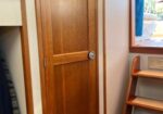 Wooden interior door in a boat cabin, with a round knob; a small wooden ladder/steps is on the right and a person in blue near an outdoor hatch.