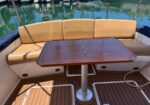 Teak-deck boat seating with a rectangular star-inlay table; water and moored boats in the background.