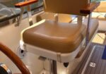 Brown captain's chair with wooden armrests on a boat deck, marina in the background