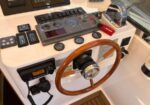 Boat helm with a wooden steering wheel, navigation screens, and engine gauges on the dashboard.