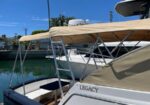 Motor yacht named Legacy docked at a sunny marina with a beige canvas cover overhead