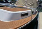 White motorboat docked at a marina with teak deck panels, stainless railing, and a beige canvas cover.