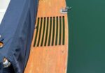Teak swim platform on a boat, with green water below and metal cleats along the edge.