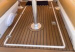 Teak cockpit deck with a central stainless pedestal, white railing frame around the edge, and deck hardware.