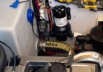 Close-up of a mechanical engine compartment showing a 24-valve engine cover, various hoses, clamps, a fuel pump, and yellow valve handles.