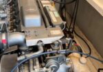 Diesel engine in a boat's engine compartment, with hoses, wiring, and a silver engine block visible beneath a wooden deck edge