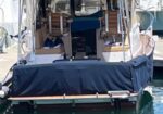Rear view of a motorboat at a marina with a blue canvas cover and tan canopy, calm water reflecting the hull.