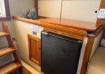 Compact boat galley with wooden countertop, cream cabinets, sink on the left, and a small fridge under the counter.