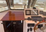 Boat helm with wooden countertop, Garmin navigation screen, steering wheel, and marina visible through cockpit windows.