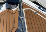 Bow of a wooden-deck boat with a chrome windlass, anchor chain, and a black cover near the dock.