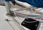 Sailboat deck with a blue sail cover, standing rigging, lines, and an open hatch under a clear deck.