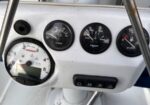 Boat helm with Edson pedestal, three small gauges (volt, temp, fuel) and a large tachometer; steering wheel and chrome rails visible.