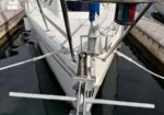 Front view of a sailboat’s bow tied to a dock, showing the anchor platform and stainless steel rails over calm water in a marina.