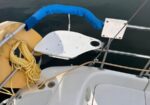 Sailboat cockpit with a blue-wrapped railing, coiled yellow rope, and a white folding table near the railing, in a calm marina with reflected boats.