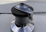Polished chrome boat winch with black grip on a white deck, close-up view.