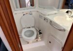 Compact boat head with a small toilet, sink, mirror, and grab bar as shown in a marine bathroom.