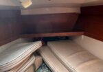 Interior of a small boat cabin with beige cushions stacked along the sides, wooden paneling, and an open skylight hatch above.
