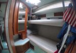 Interior of a small sailboat cabin with bunks, wooden cabinets, and an American flag nearby.