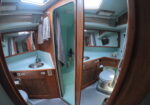 Boat bathroom interior with wooden cabinetry, teal walls, a sink, mirror, and towels hanging nearby; small skylights above. - Informative image inside a boat.