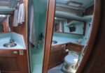 Interior of a small boat bathroom with wood cabinets, teal walls, and a frosted glass shower door between sink and toilet area.