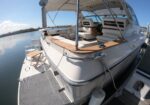 White luxury motor yacht docked at a marina with open rear deck and white cushioned seating under a canopy, calm water nearby.