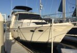 White motor yacht moored at a marina, with rigging and a clear blue sky above.