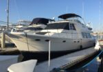 Large white motor yacht docked at a marina, upper deck with dark blue canopy and clear blue sky.