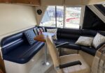 Cozy yacht salon with navy leather seating, nautical pillows, and a wooden table; marina visible through the window.