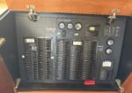 Cockpit electrical panel with numerous labeled switches, gauges, and an Onan GenSet unit at center-right, viewed from above with open blue panels around.