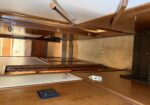 Narrow wood-paneled cabin hallway on a boat, stairs at the bottom and a bed with a dresser visible at the far end.