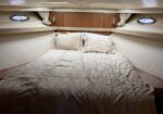 Bed in a luxury yacht cabin with beige patterned bedding, wooden storage, and round porthole windows on each side