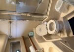Compact boat bathroom with toilet, sink, tissue box on shelf, towel bar, and glass shower enclosure with chrome trim
