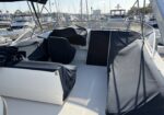 Deck of a motorboat with dark navy canvas covers over seating, overlooking a marina full of sailboats and yachts.
