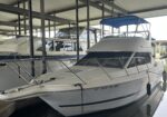 White motor yacht with a blue canopy docked in a covered marina, metal supports around.