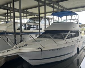 White motor yacht with a blue canopy docked in a covered marina, metal supports around.