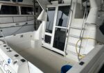 Cockpit deck of a white motorboat with a glass cabin door, metal railings, and a blue bucket on the deck.