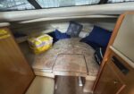 Boat cabin interior with beige cushioned seating, blue pillows, and a yellow bag on the berth.