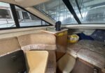 Boat interior cabin with beige upholstered seating, a small fan on a wooden cabinet, and large windows with blinds?