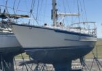 White sailboat on stands in a boatyard, masts and lines towering overhead against a clear blue sky