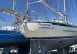 Sailboat named Paloma, Wilmington, DE, on a dry dock with masts and rigging visible against a blue sky.