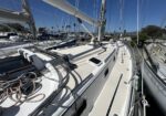 Close-up view of a sailboat deck with ropes and rigging, masts and neighboring boats at a sunny marina.