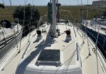 View forward from the cockpit of a sailboat, with rigging, lines, and hatches on the deck and neighboring boats nearby.