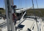 Close-up of sailboat deck with ropes, winches, and a white boom against a blue sky.