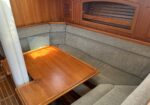 Wood-paneled boat cabin with an L-shaped gray upholstered seating area and a polished wooden table.