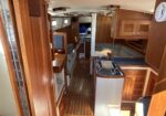 Wood-paneled sailboat cabin with galley, seating area, and overhead storage fixtures visible along the ceiling.