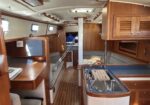 Sailboat interior with wooden cabinetry, a galley sink, and cushioned seating along the walls under small porthole windows.