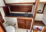 Boat bathroom vanity with dark countertop, stainless sink, chrome faucet, and tall wooden cabinet; toilet visible nearby.